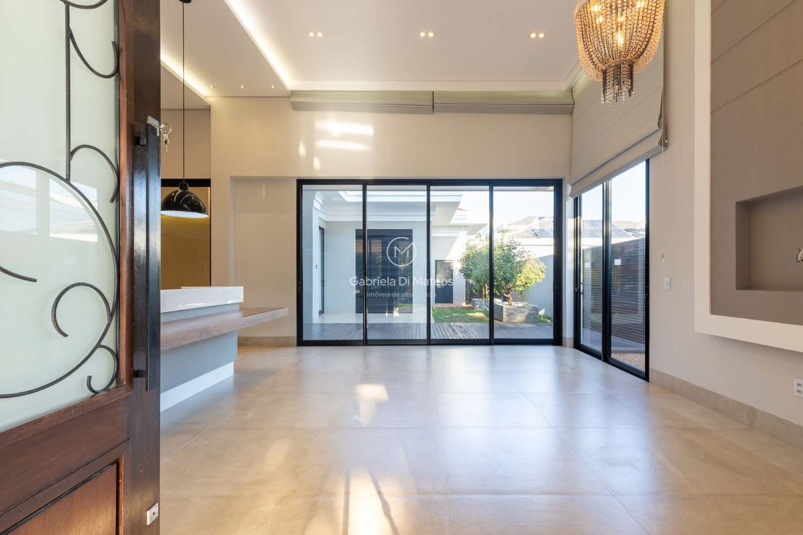 Sala integrada com porcelanato claro, pé-direito alto e esquadrias de alumínio preto voltadas para o jardim